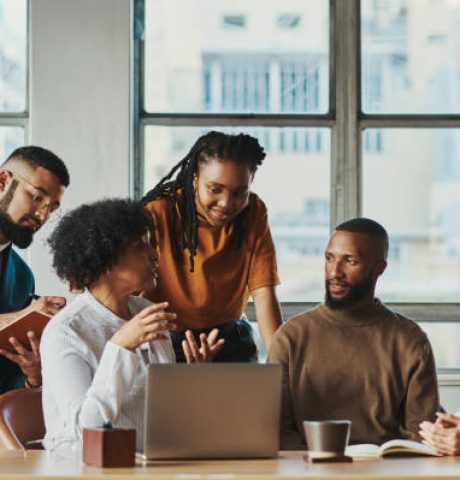 Five business people sit around a desk in an office with a laptop on while having a strategic business meeting. Stock photo